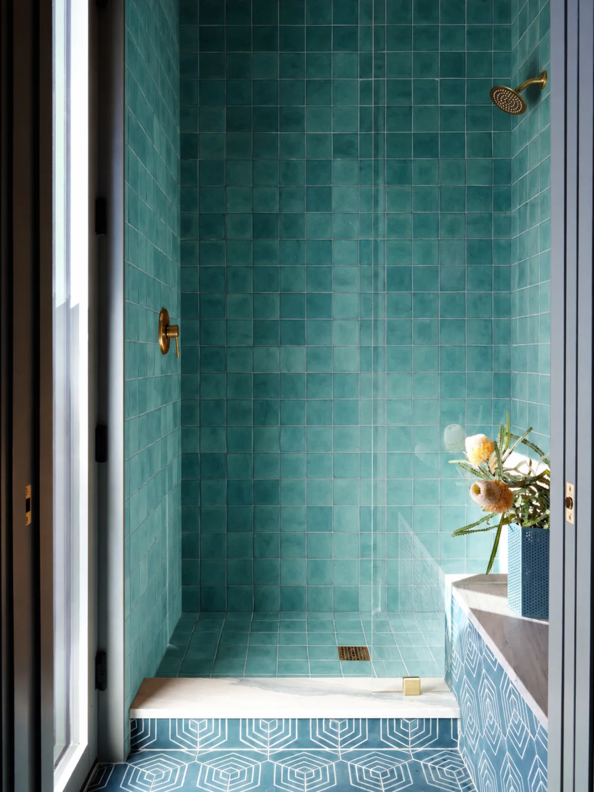 Hotel shower lined in teal glazed tile with brass fittings and a patterned floor
